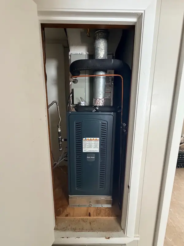 American Standard gas furnace installed in a closet, with the insulated refrigerant lines, flue pipe and gas line connected above and beside it
