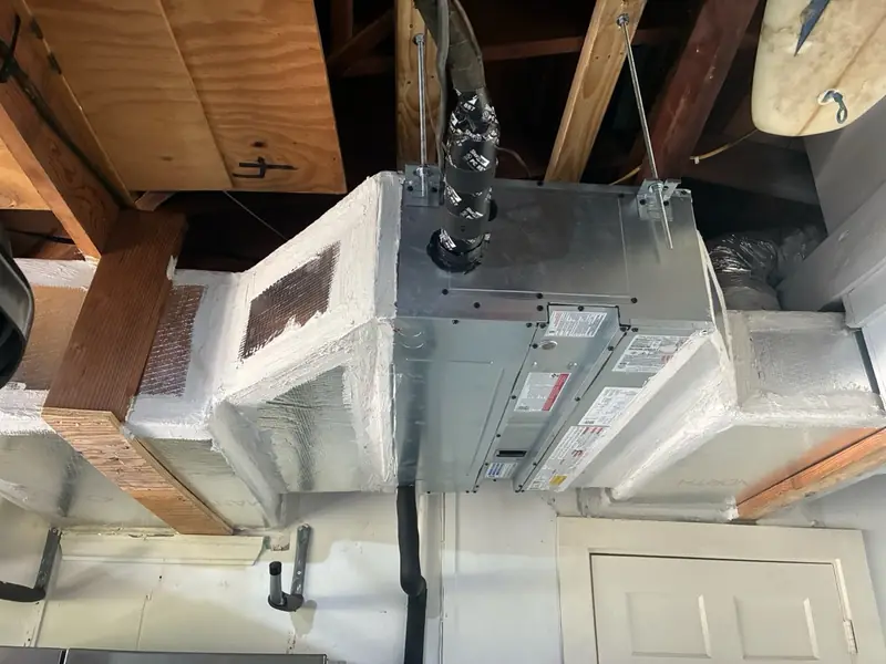Custom sheet-metal plenums and trunk, sealed and wrapped in insulation, around an indoor unit hung on threaded rods